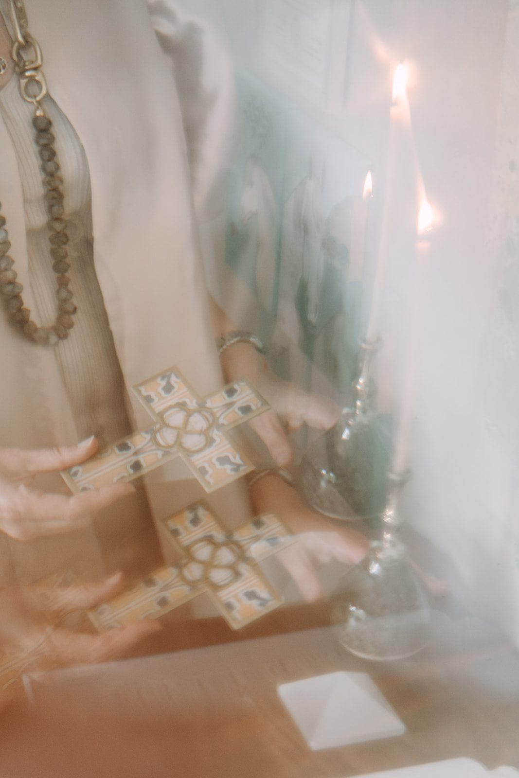 Hands holding an ornate cross beside a lit candle